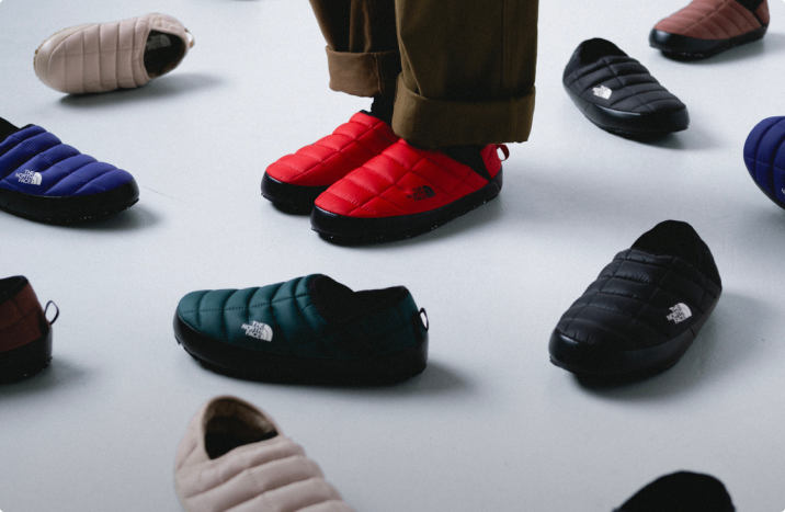 A person wearing red Thermoball Mules surrounded by scattered Thermoball mules.