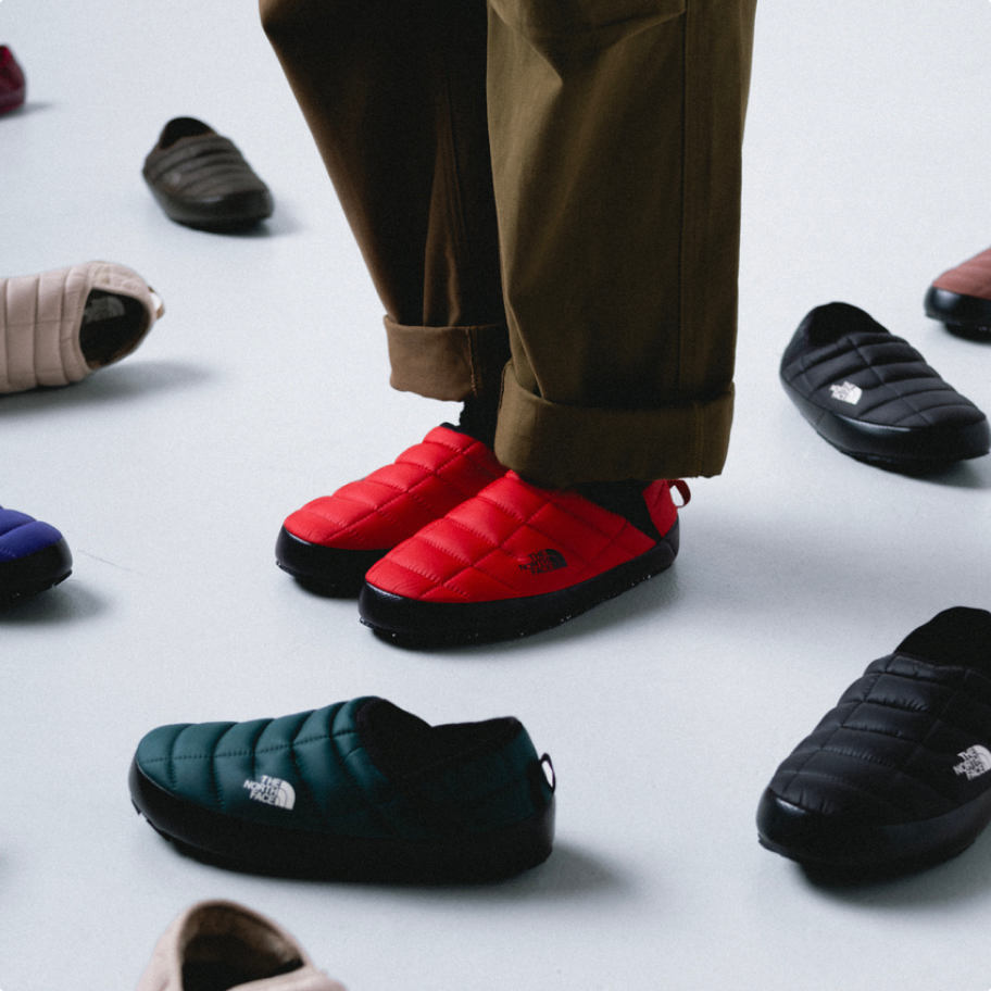 A person wearing red Thermoball Mules surrounded by scattered Thermoball mules.