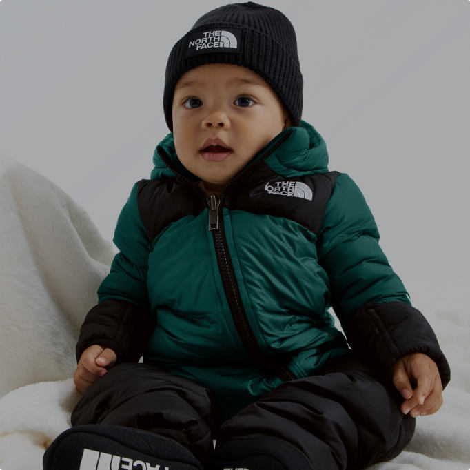 A baby wearing a teal jacket and black beanie from The North Face.
