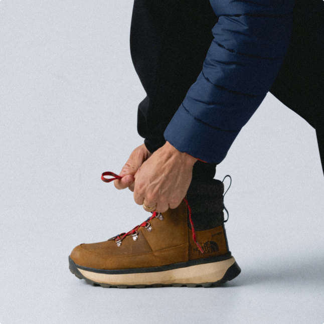A person tying brown winter boots.
