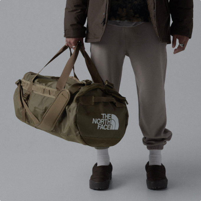A man carrying a tan Basecamp Duffel bag.