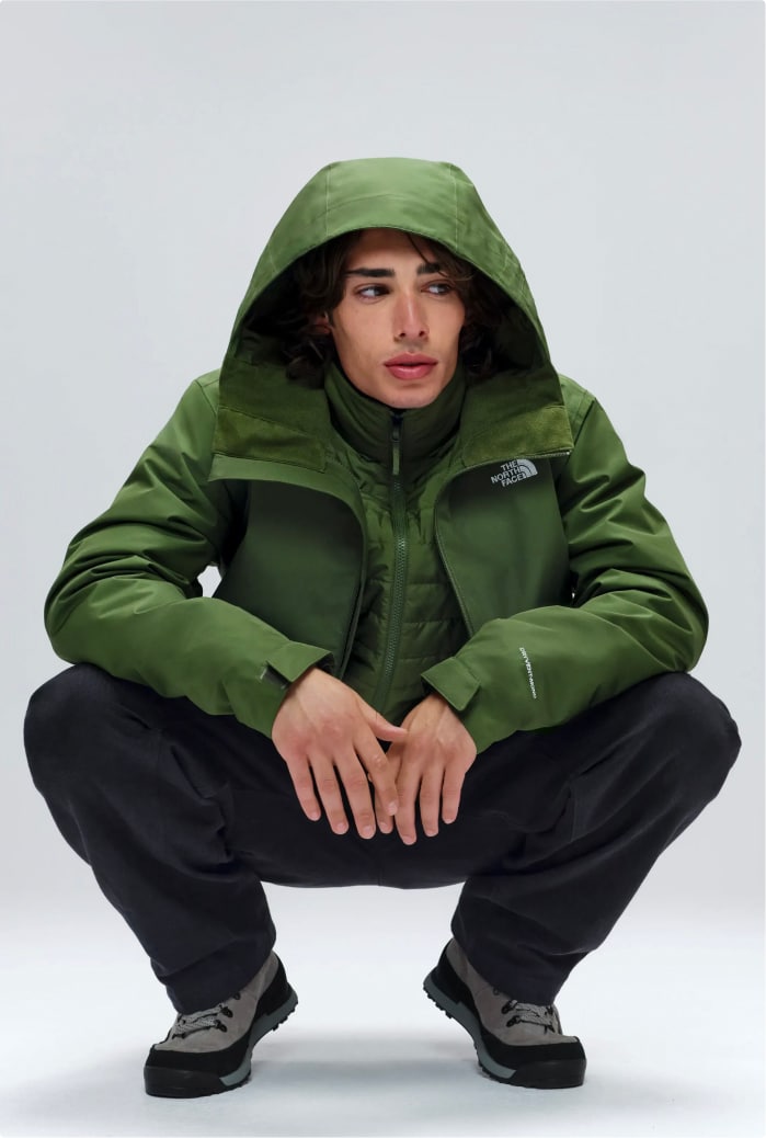 Man crouched down wearing a bright green hooded jacket and black pants.