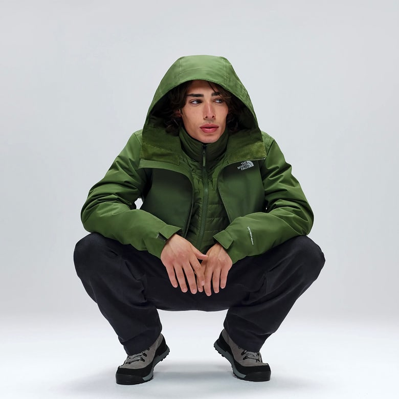 Man crouched down wearing a bright green hooded jacket and black pants.