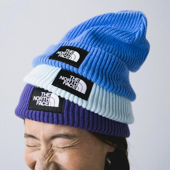 Close-up of woman squinting and wearing three beanies (sky blue, light blue and purple) stacked on top of each other.