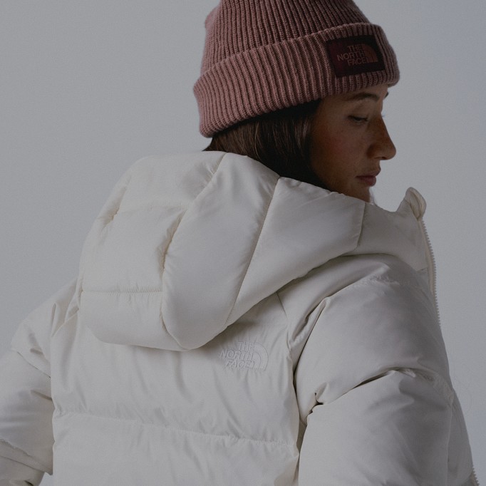 A woman's back facing the camera wearing a white insulated jacket and a pink beanie