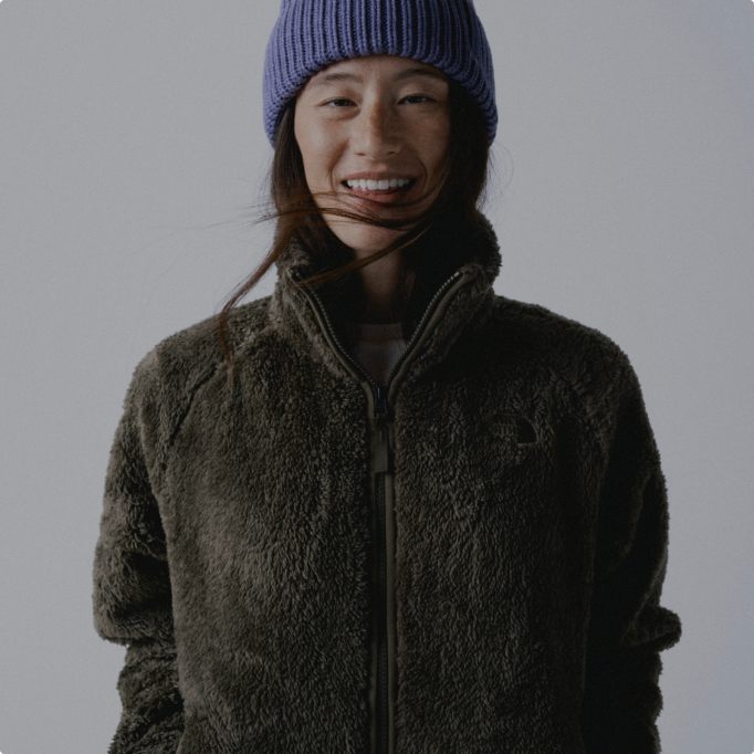 A woman smiling wearing a green osito evolve jacket and a purple beanie