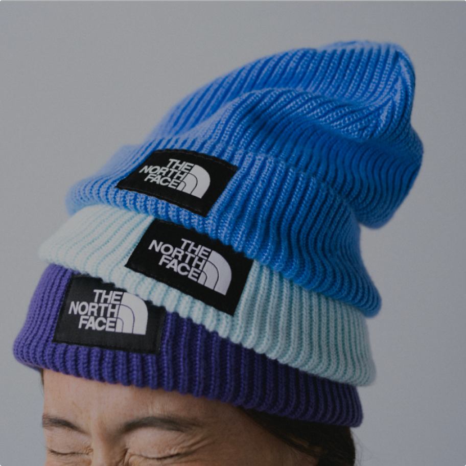 Close-up of woman squinting and wearing three beanies (sky blue, light blue and purple) stacked on top of each other.