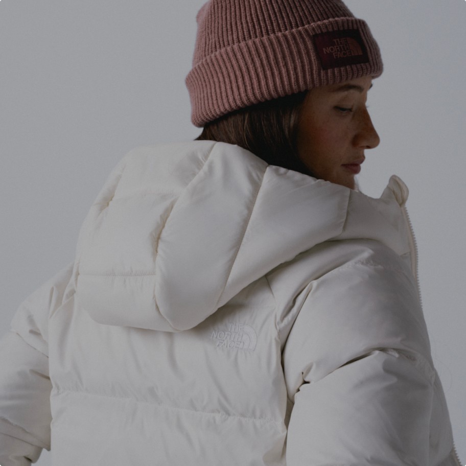 A woman's back facing the camera wearing a white insulated jacket and a pink beanie