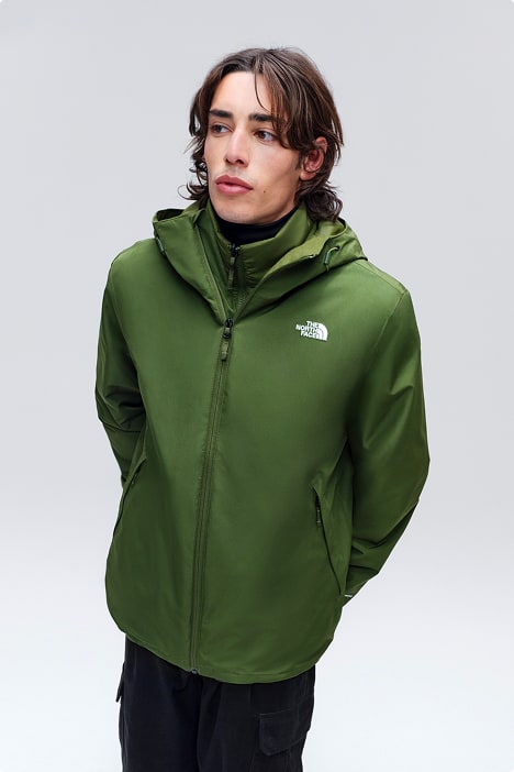Man with brown mid-length hair wearing kelly green jacket zipped up with his arms behind his back against white background.