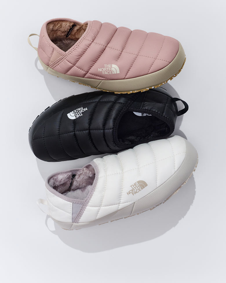 Three pairs of slippers starting from top: pink, black and white, against white background.
