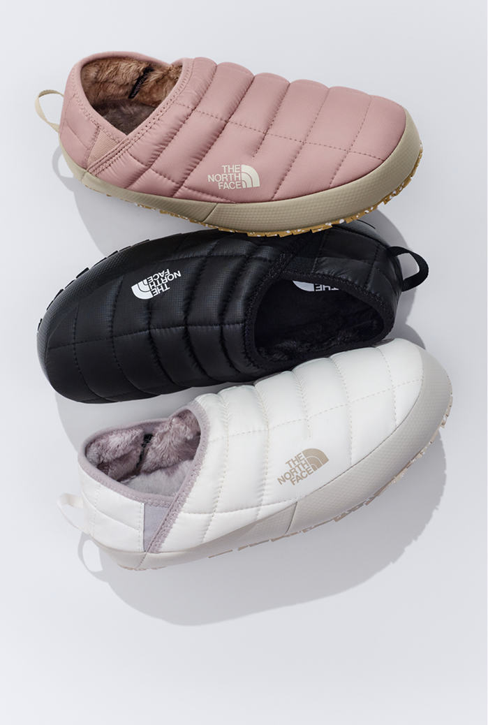 Three pairs of slippers starting from top: pink, black and white, against white background.