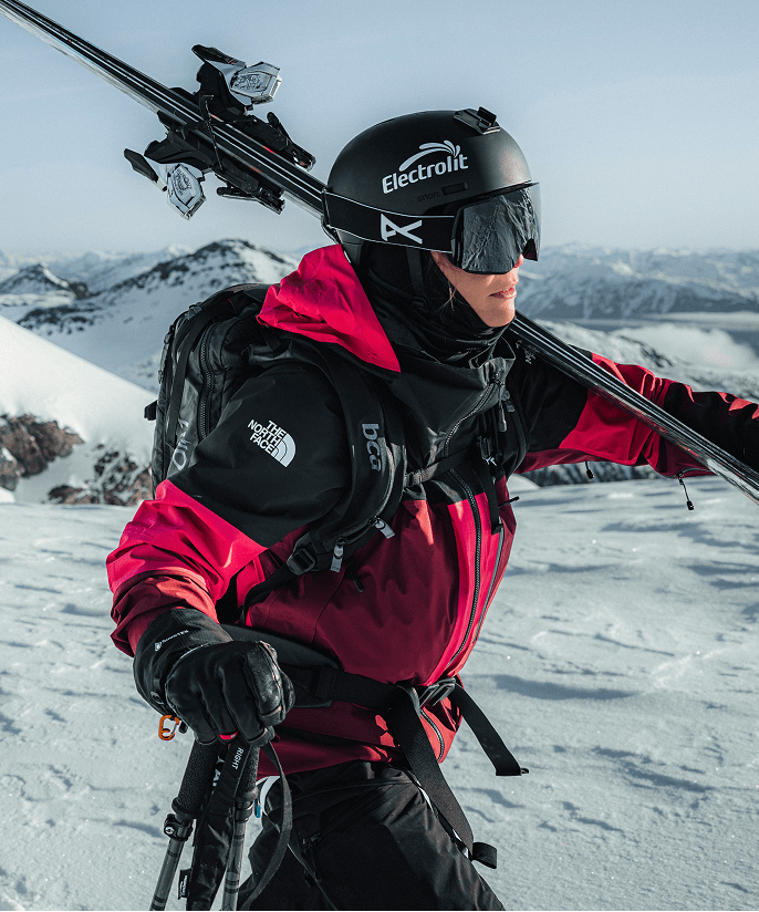 Photo of a woman carrying skis over her shoulder on a snow-covered mountain ridge wearing Summit Series outerwear.