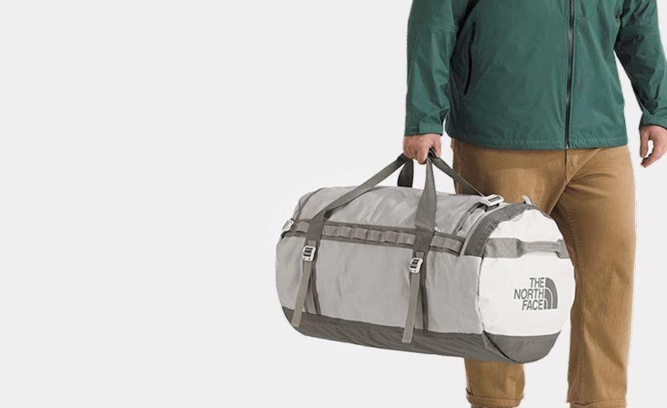 A studio shot of someone carrying a Base Camp Duffel by the handles. 