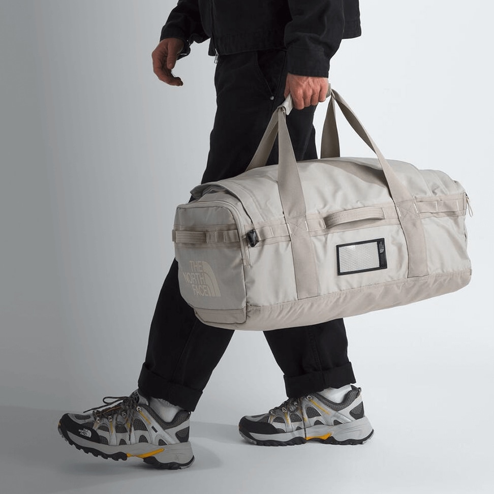 A studio shot of someone carrying a Base Camp Voyager Duffel by the handles.