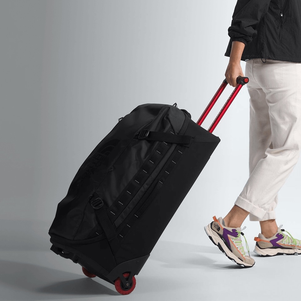 A studio shot of someone wheeling the Base Camp Rolling Thunder luggage.