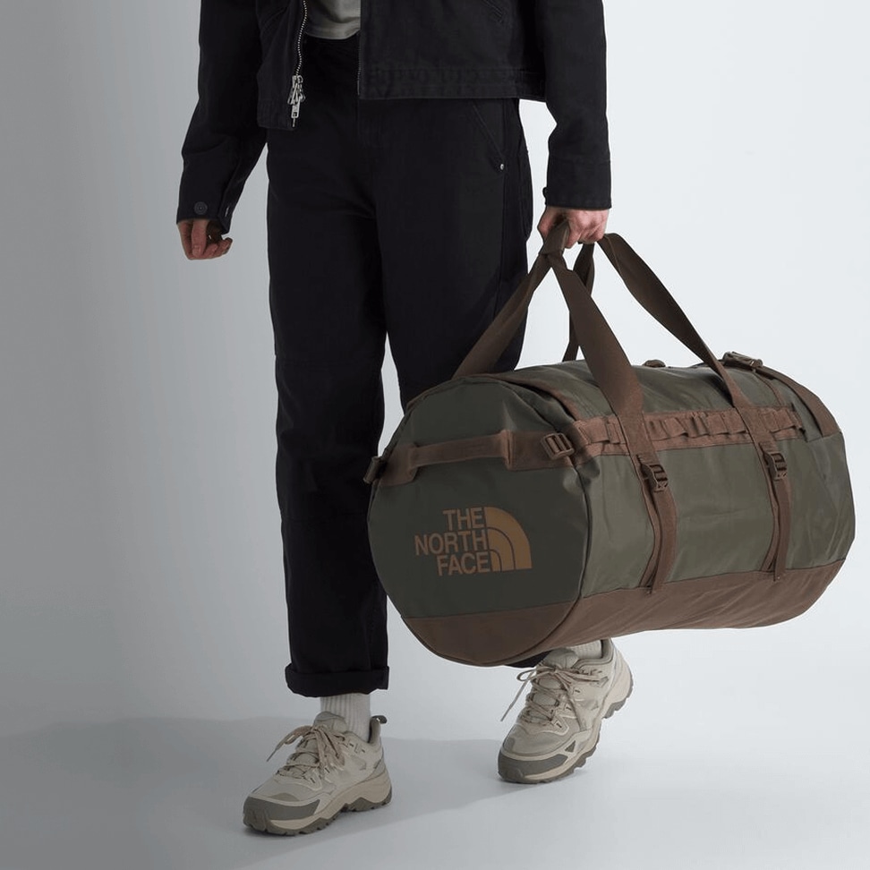 A studio shot of someone carrying a Base Camp Duffel by the handles.