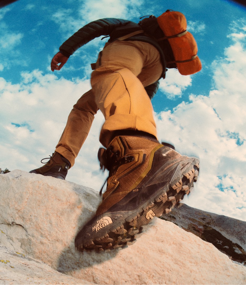 A man stepping onto a rock wearing brown hiking boots paired with brown pants. 