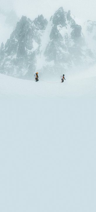 Two people tethered together with a rope walking through snow with an epic peak in the background.