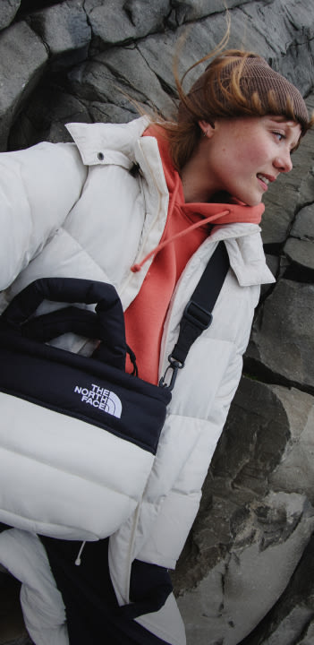 A woman in a white jacket standing against a rock wall. She's looking away from the camera. 