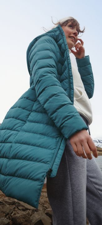 A woman in a white hoodie/white beanie/turquoise jacket with her arms stretched out. 