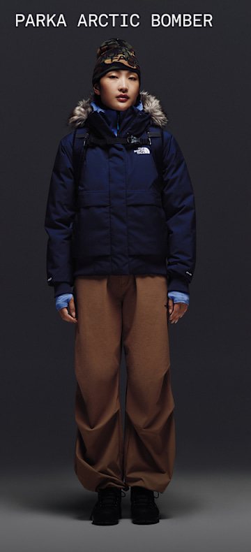 Female model wearing The North Face Arctic Bomber in Summit Navy with fur-trimmed hood, styled with brown snow pants