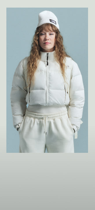 A woman in a white beanie and matching Nuptse, the image has a white frame around it.