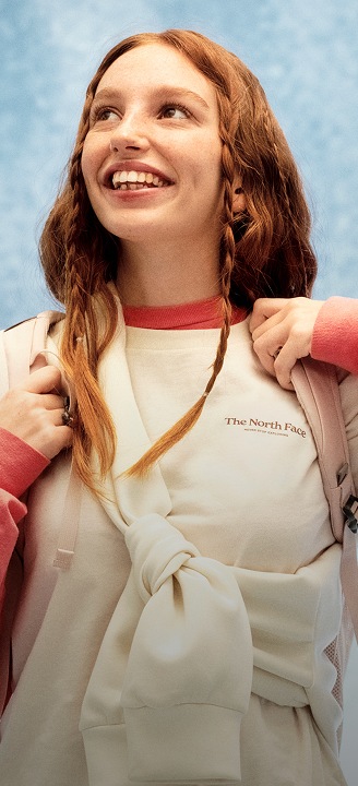 Young woman in a white shirt and orange long sleeve looking happy.