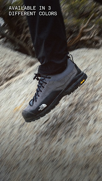 A person’s legs are in motion, wearing black Verto Approach Shoes walking on a rocky surface.