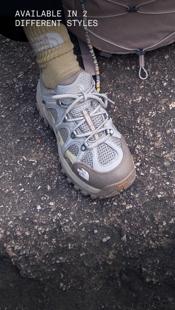 A person is resting their legs on a rock, only the bottom half of the legs are shown, wearing gray Hedgehog 06 RVST Shoes.