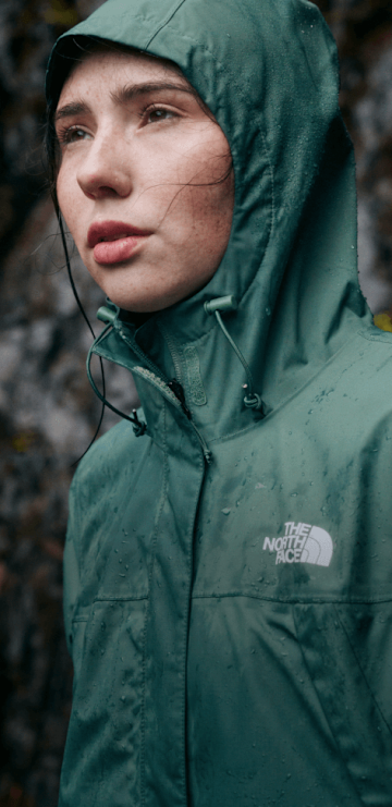 A woman in a green rain jacket with the hood up looking to the left.