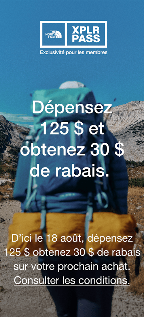 Une photo de la personne par derrière, elle porte un sac à dos bleu avec des accents turquoise et un chapeau blanc qui marche vers les montagnes. 