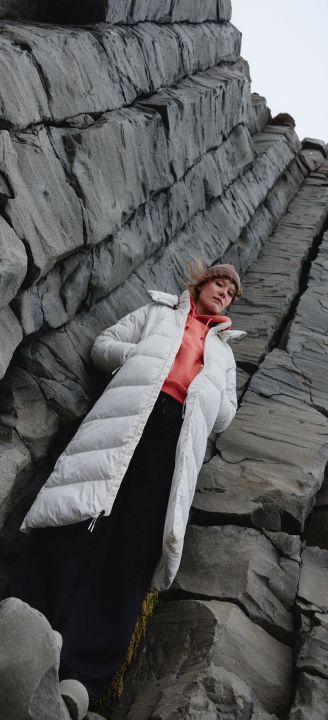 A person in a white jacket standing against a rock wall.