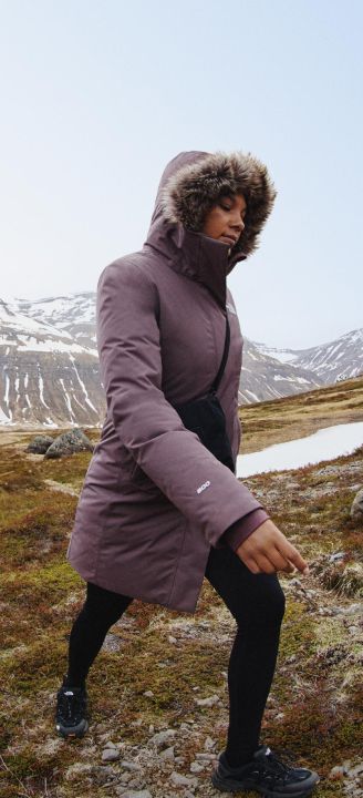 A woman in a purple jacket walking in nature with her hood up.