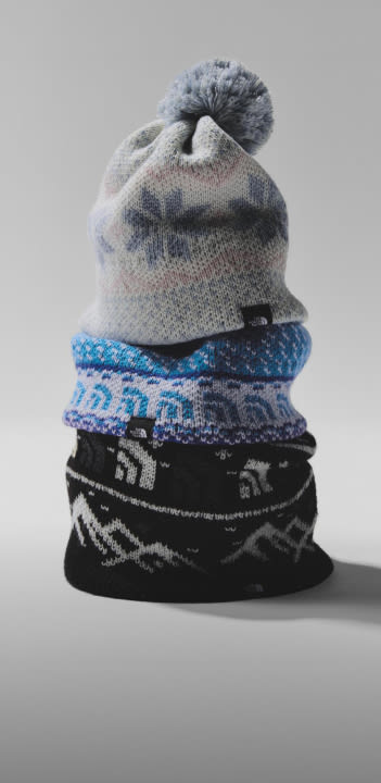 Stacked beanies with a grayish/whiteish beanie with snowflakes and a pom pom on top. 