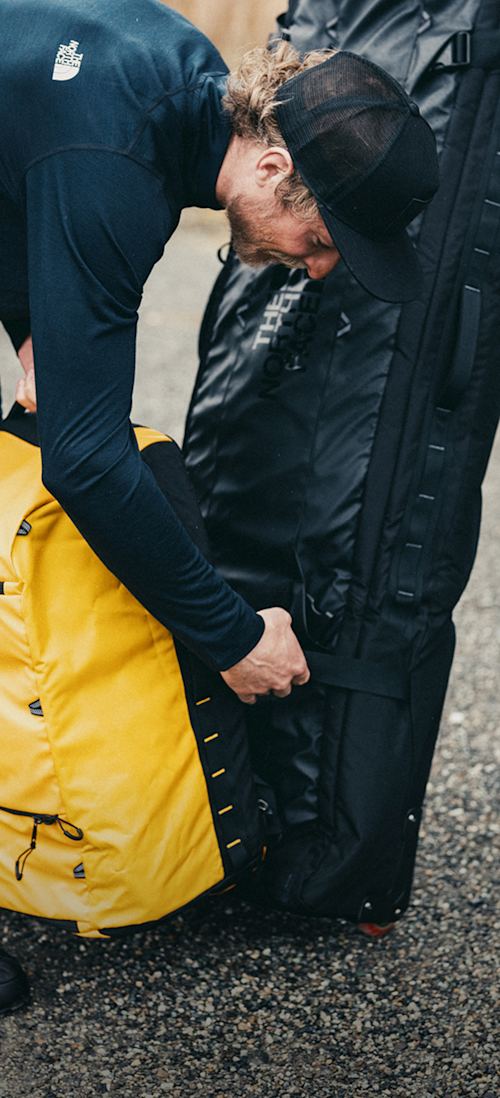 Two people walk toward the slopes, carrying The North Face Base Camp Boot Pack in Summit Gold and Base Camp Snow Roller. 