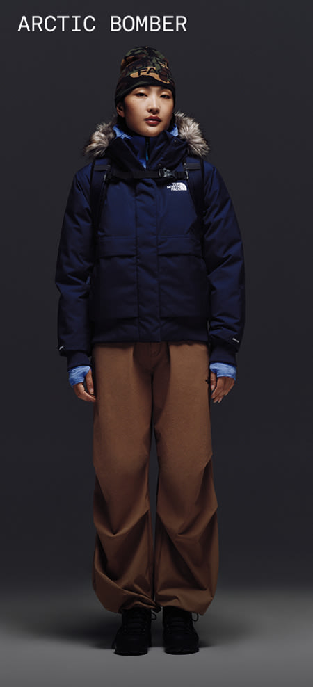 Female model wearing The North Face Arctic Bomber in Summit Navy with fur-trimmed hood, styled with brown snow pants