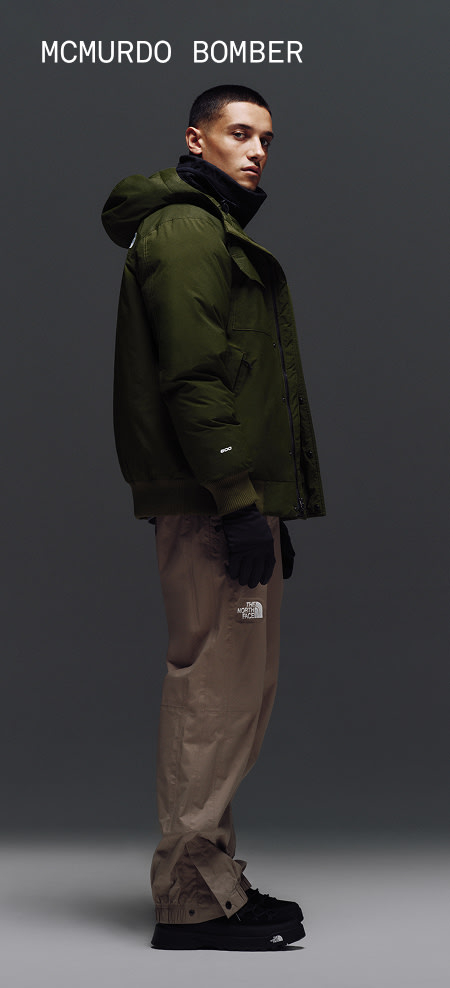 Male model wearing The North Face McMurdo Parka in Woodland Green against a gray studio background. 