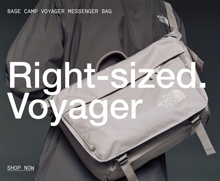 A person wearing a white/taupe messenger bag with a green jacket. 