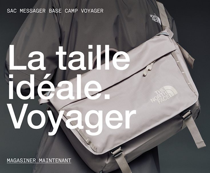 A person wearing a white/taupe messenger bag with a green jacket. 