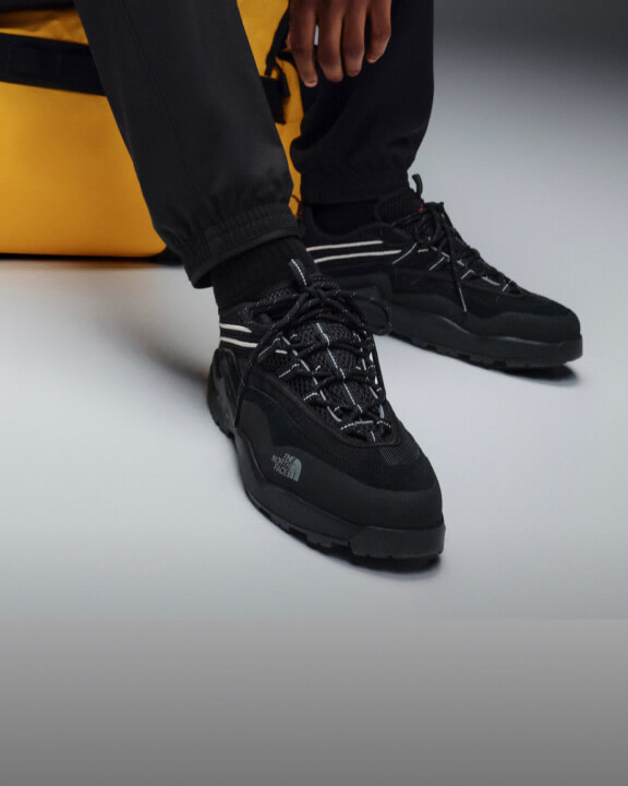 Model seated wearing The North Face Clyffe Ultra Shoes in TNF Black with black pants