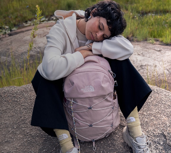 Young woman sitting on rock resting with her pink backpack.