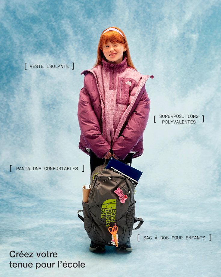 Un enfant vêtu d’un molleton et d’un manteau violet, tenant un sac à dos, qui regarde l’appareil photo en fermant un œil.