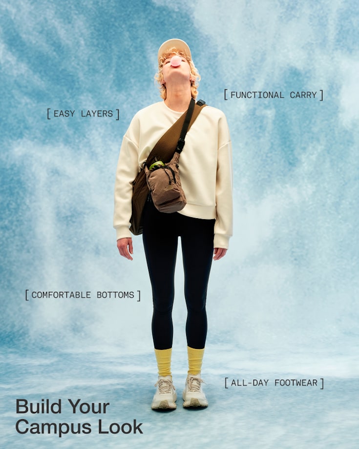 Person in an off-white sweatshirt, black pants, yellow socks, white shoes and wearing a brown sling bag, looking upward and blowing a bubble with bubblegum.