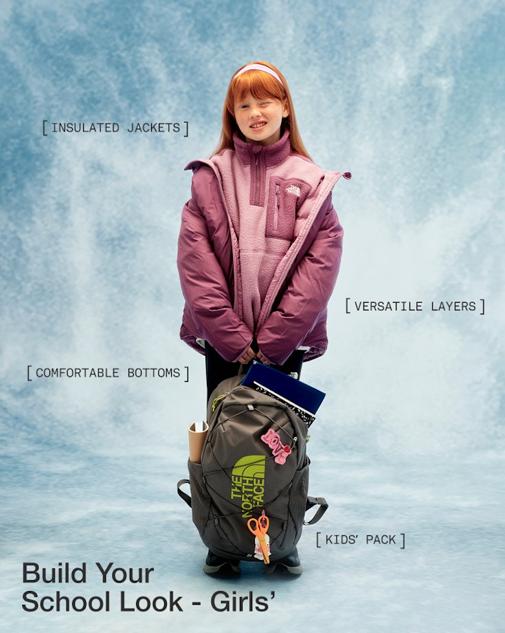 A child wearing a purple fleece and purple jacket, holding a backpack, looking at the camera with one eye closed.