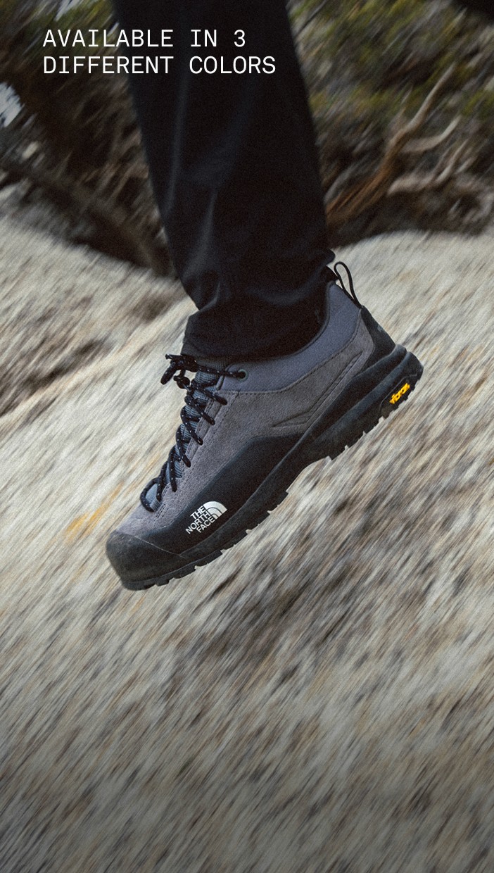 A person’s legs are in motion, wearing black Verto Approach Shoes walking on a rocky surface.