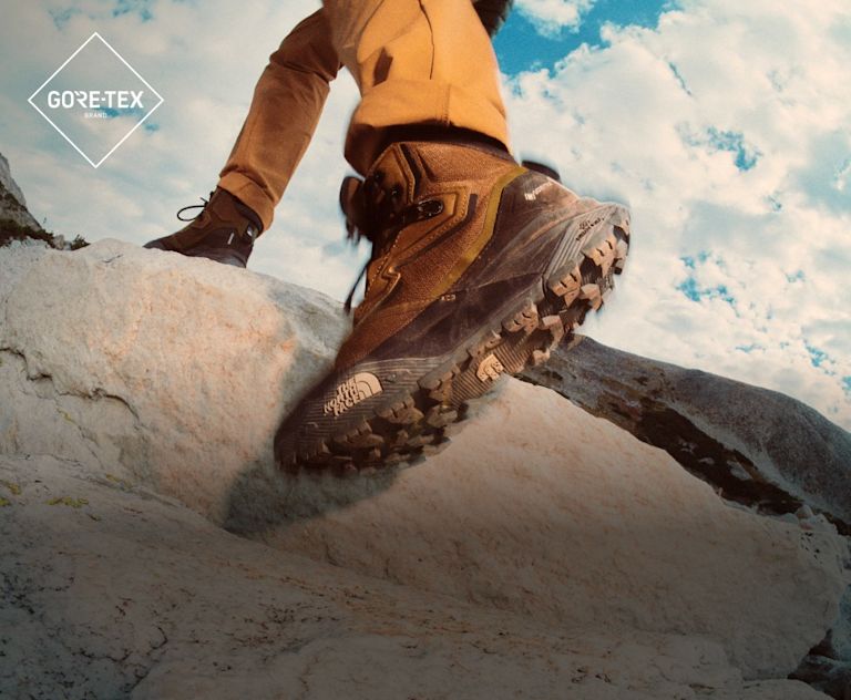 A woman wearing low-rise, tan hiking shoes with black and gray socks. She’s scaling red rocks.