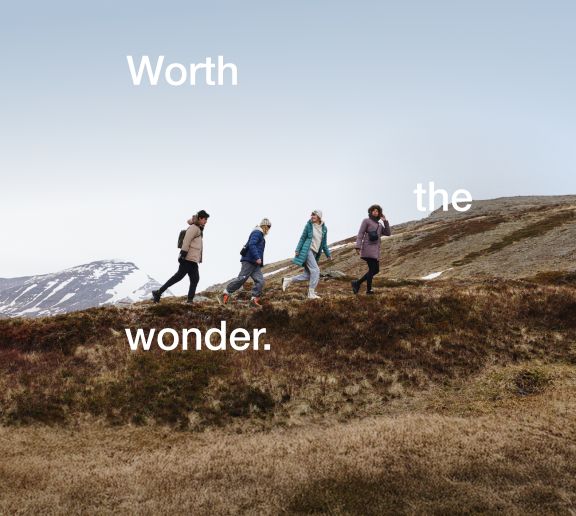 Four people walking across a grassy ridge. From left to right: Tan jacket, navy jacket, turquoise jacket, purple jacket. 