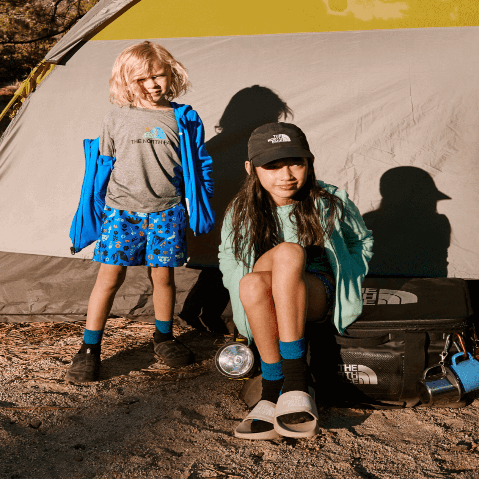 Deux enfants devant une tente, portant des articles North Face.
