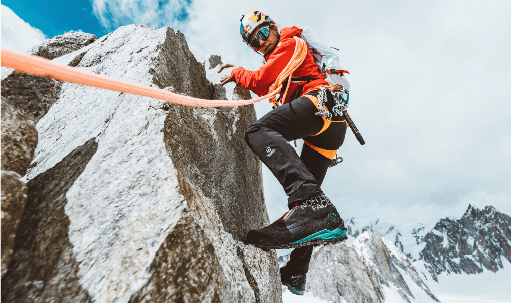 a man is pictured wearing north face mountaineering boots while scaling a large rock in winter conditions