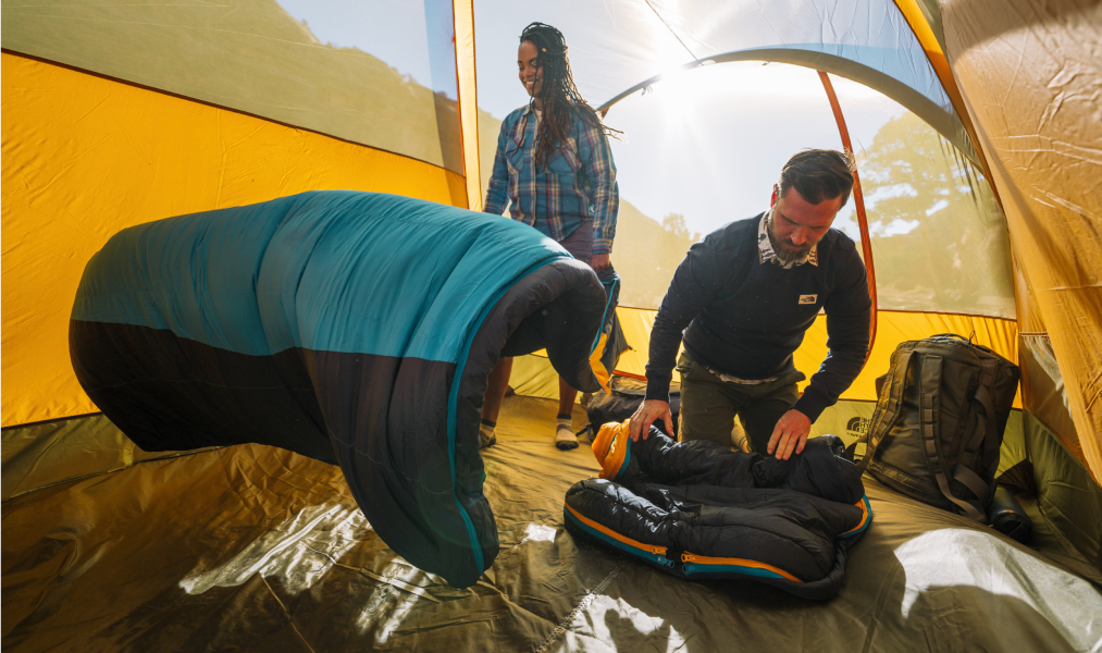 two people in a tent setting up their north face sleeping bags